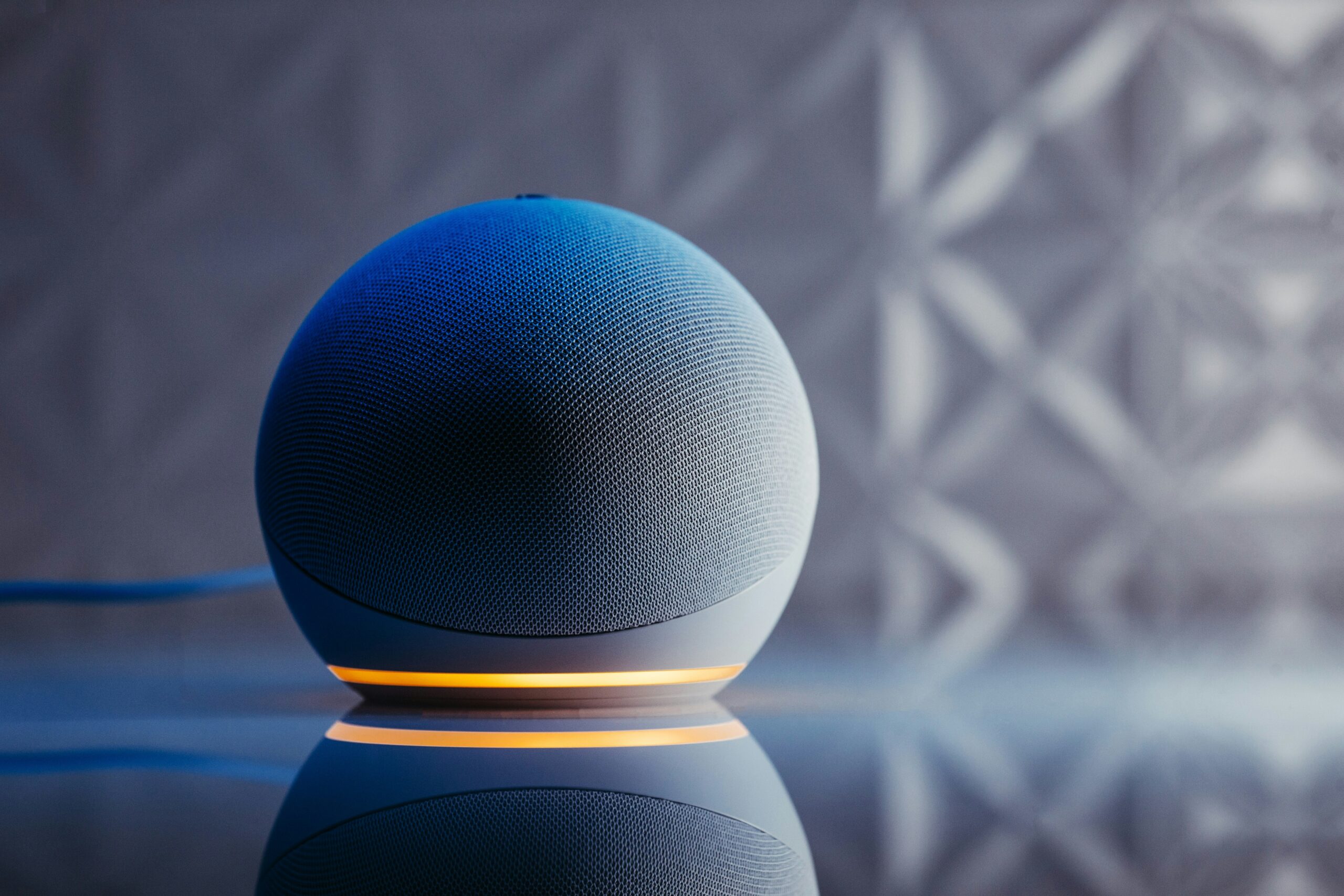 An Amazon Alexa smart speaker in blue and orange, reflecting on a surface, highlights voice search technology for SEO optimization.