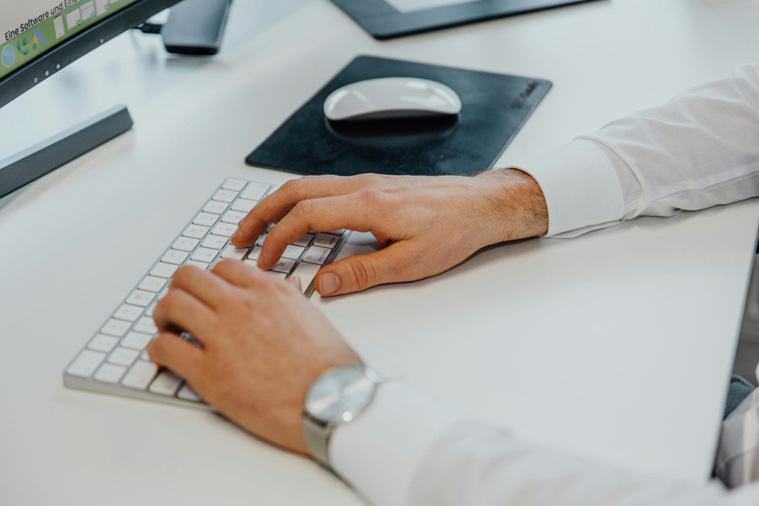 A professional male hand typing on a white Apple keyboard on a modern desk setup, with a curved monitor displaying Google E-E-A-T SEO guidelines, a wireless mouse on a black pad, and a drawing tablet nearby, demonstrating expertise in search engine optimization.