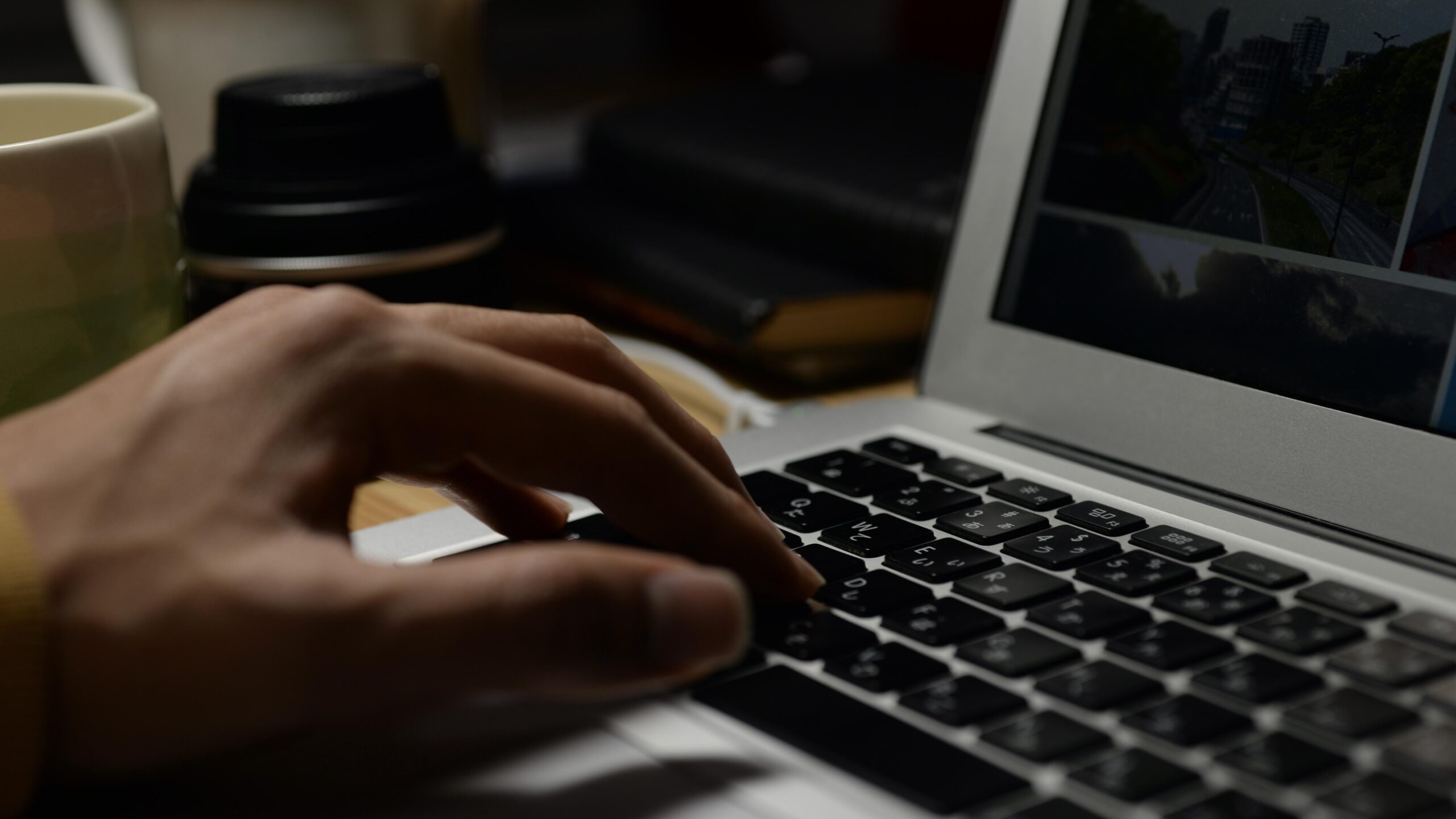 A person typing on a laptop keyboard late at night, with a coffee mug and thermos nearby, displays a webpage with cityscapes, which symbolize content creation and SEO optimization.