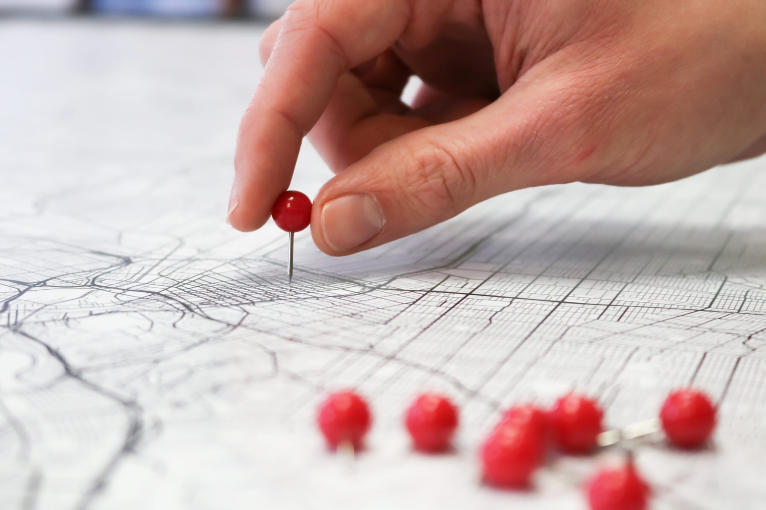 A hand places a red push pin on a detailed city map, symbolizing local business location marking for local SEO, with additional red push pins scattered nearby.