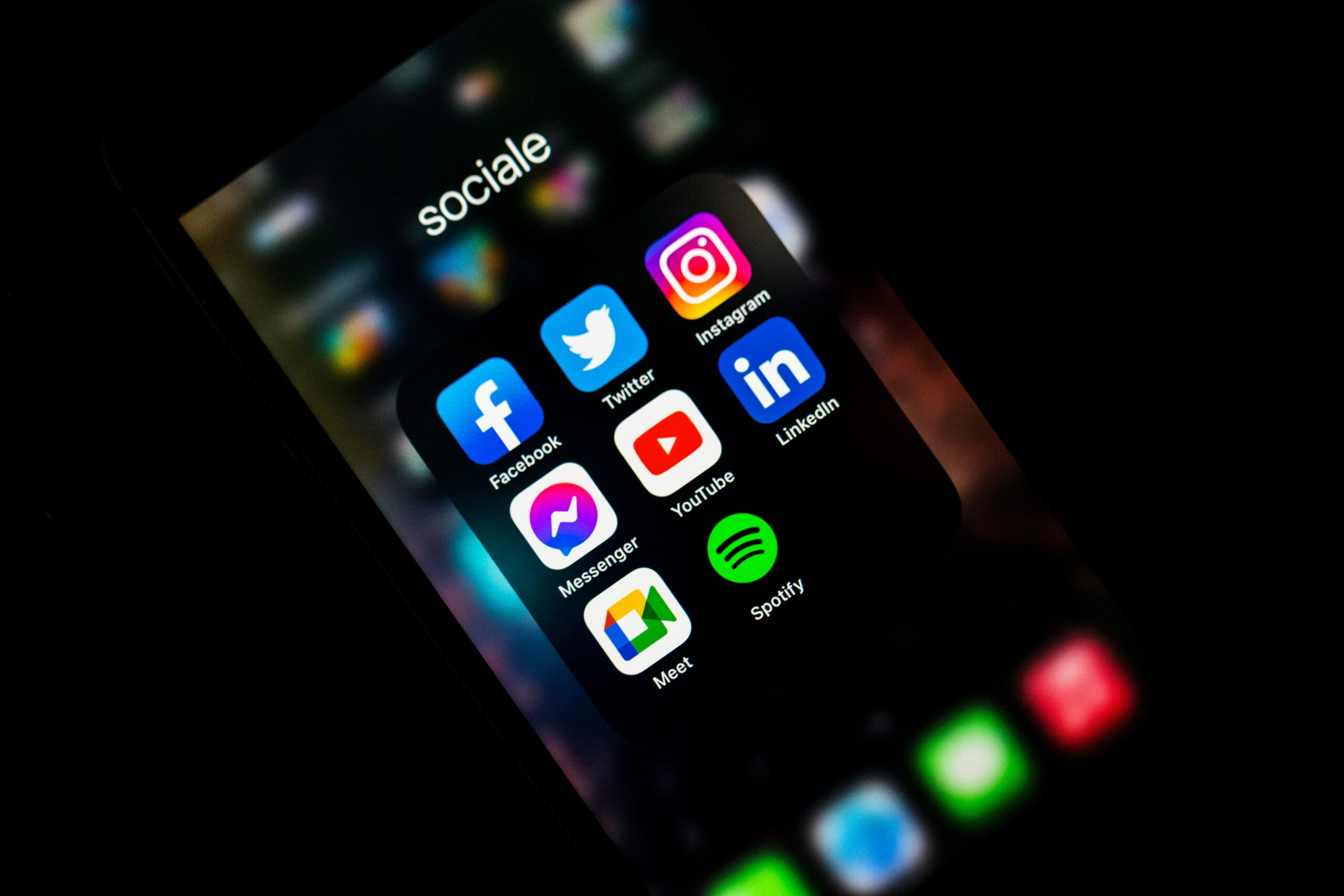 Popular social media app icons such as Facebook, Twitter, Instagram, LinkedIn, YouTube, Messenger, Spotify, and Meet are displayed on a smartphone screen against a dark background.